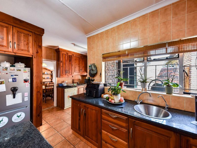 A functional kitchen featuring warm wooden cabinetry, granite countertops, a stainless steel sink, and tiled backsplash, with an adjacent view into the dining area.
