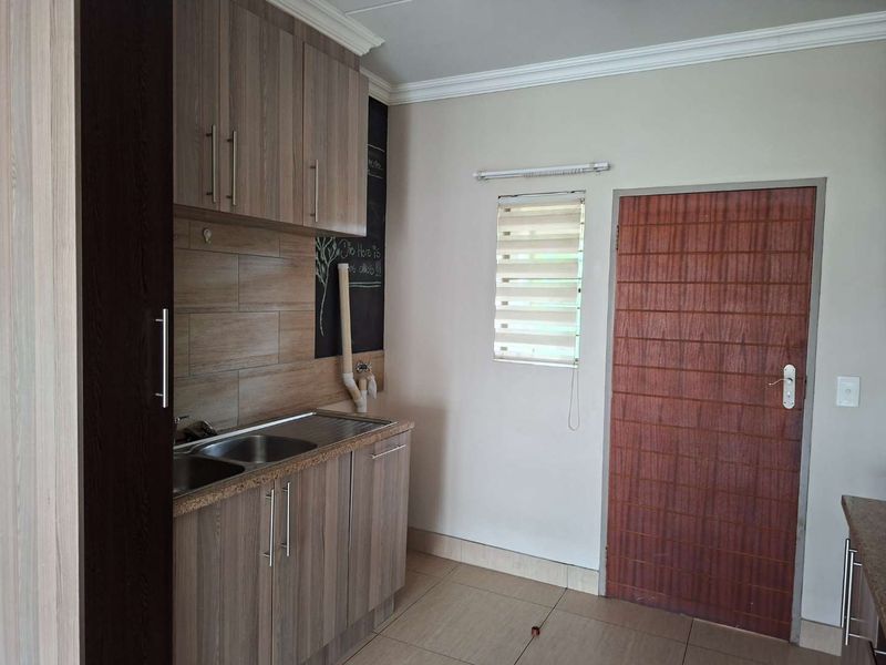 A functional kitchen area featuring wood-look cabinetry, a stainless steel sink, tiled backsplash, and neutral floor tiles.