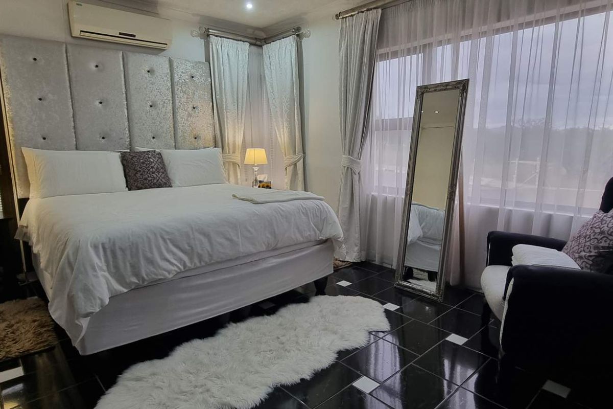 A well-maintained bedroom featuring dark tiled flooring, a wall-mounted air conditioning unit, and large windows with sheer curtains.