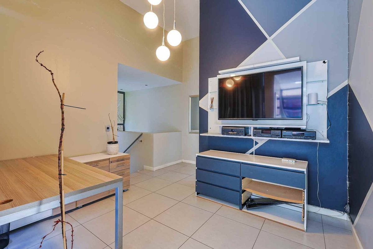 A living area featuring tiled flooring, a feature wall with geometric paint, and a built-in media unit with integrated shelving.
