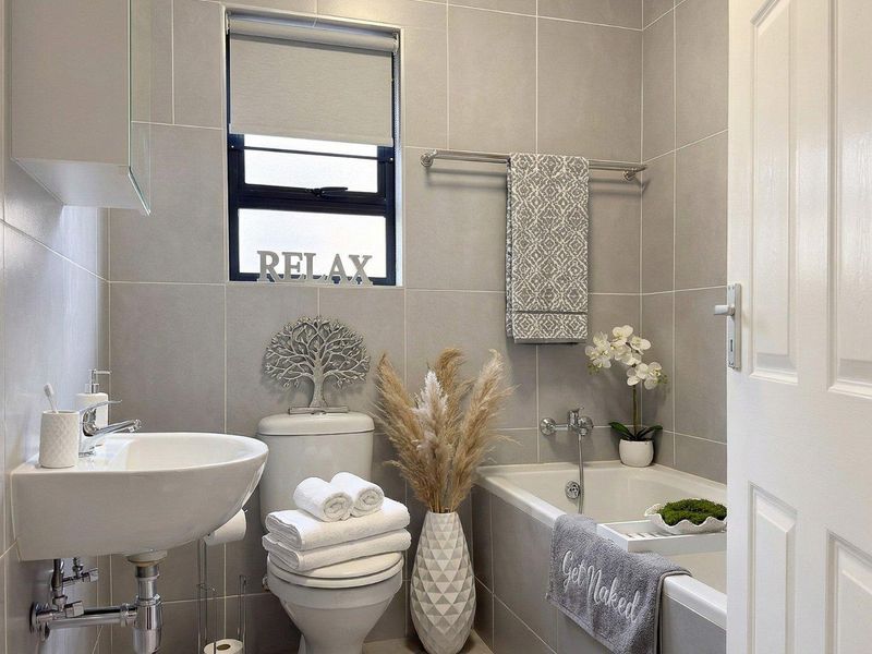 A modern, well-maintained bathroom featuring floor-to-ceiling grey tiling, a wall-mounted basin, a toilet, and a bathtub with chrome fixtures.