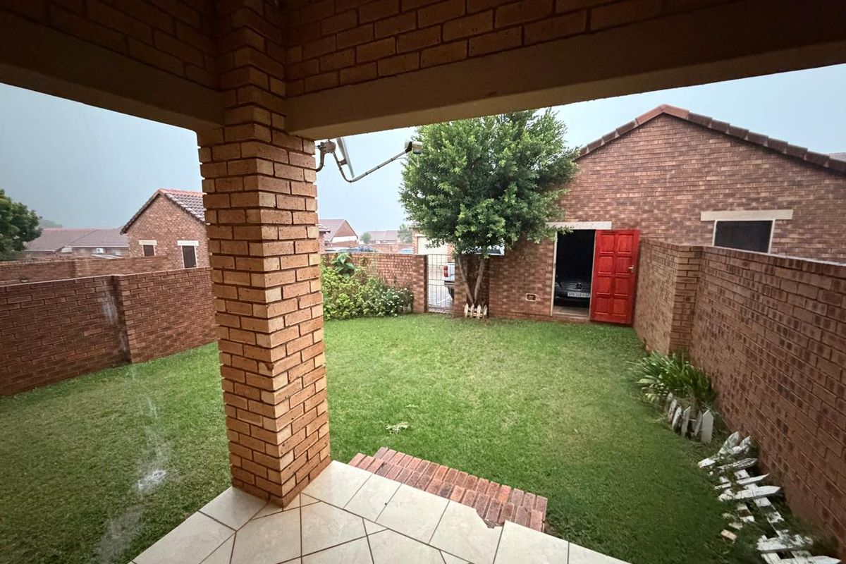 A private rear garden featuring a covered patio, brick boundary walls, and a small lawn area with access to a garage.