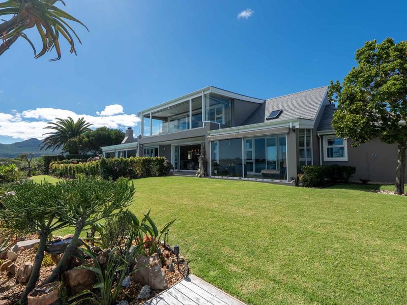 A well-maintained rear exterior view of the house featuring a landscaped garden, large glass sliding doors, and an upper-level balcony with glass balustrades.