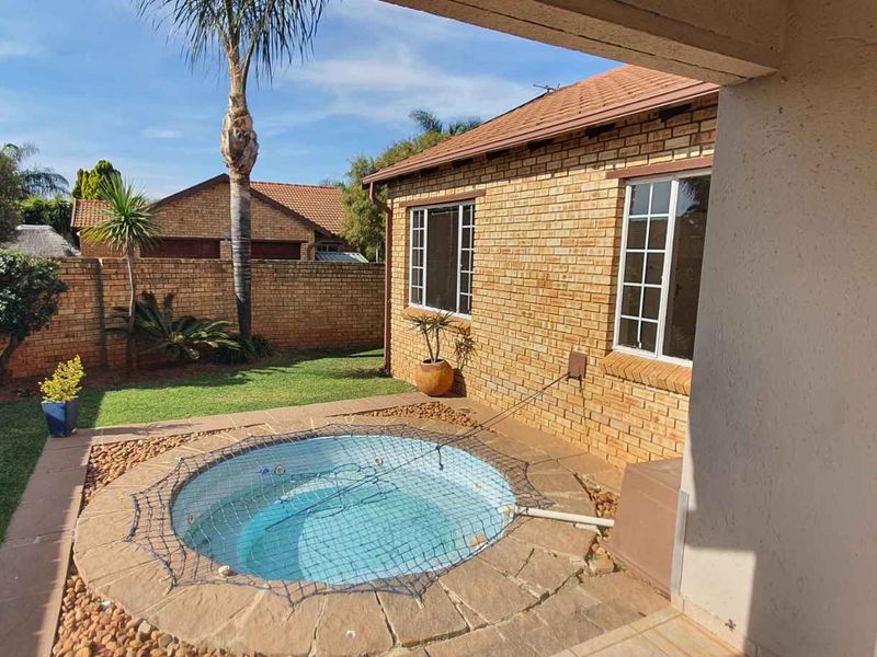A private rear garden featuring a built-in circular swimming pool with stone coping, set against a brick townhouse facade and a covered patio area.