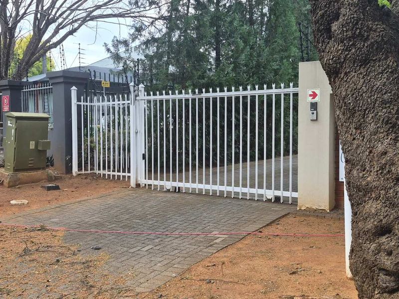 Front entrance of the office property featuring a secure gated driveway, perimeter fencing, and paved access point.