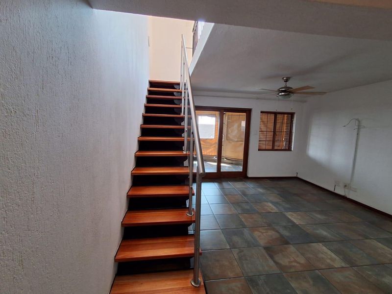 Open-plan living area featuring a modern wooden staircase with metal railing, tiled flooring, ceiling fan, and access to an outdoor balcony through sliding doors.