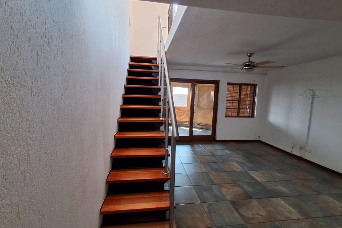 Open-plan living area featuring a modern wooden staircase with metal railing, tiled flooring, ceiling fan, and access to an outdoor balcony through sliding doors.
