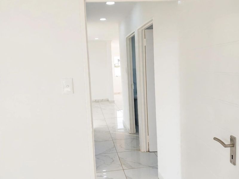 A bright, minimalist hallway featuring modern marble-look floor tiles and recessed downlighting, connecting multiple rooms within the home.
