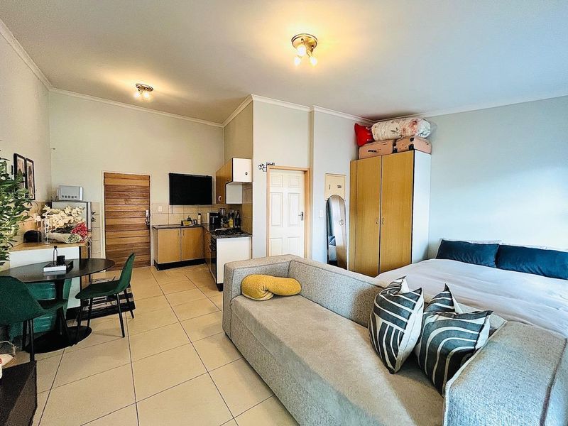 An open-plan studio apartment featuring tiled flooring, a compact kitchenette with built-in cabinetry, and a built-in wardrobe, offering a functional living and sleeping space.
