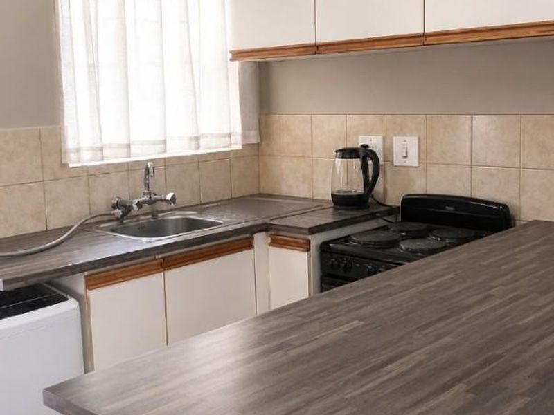 A functional kitchen featuring laminate countertops, tiled backsplash, built-in cabinetry, and an electric stove with a stainless steel sink.