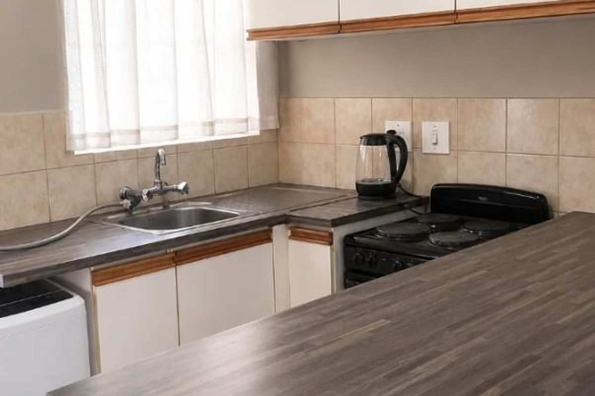 A functional kitchen featuring laminate countertops, tiled backsplash, built-in cabinetry, and an electric stove with a stainless steel sink.