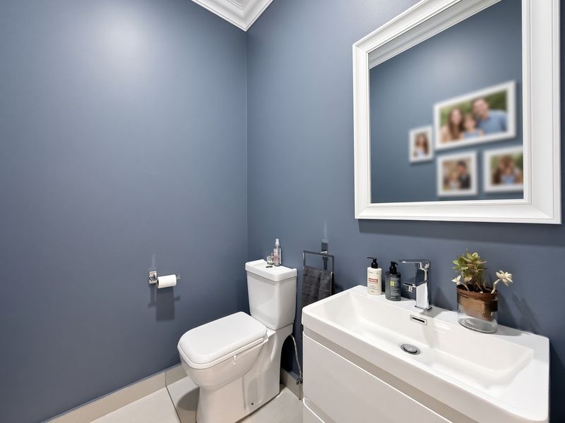 A modern powder room featuring a sleek white vanity, basin, and toilet against a contemporary blue wall finish.