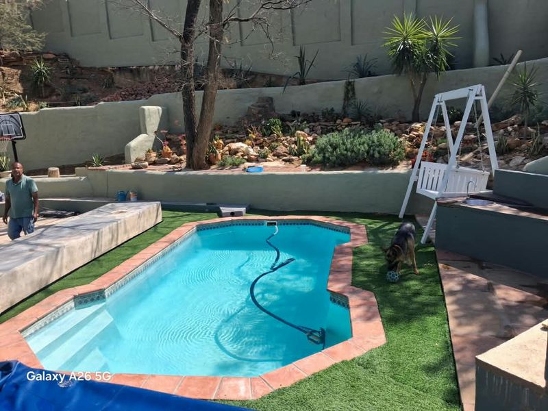 Outdoor pool area featuring a swimming pool with terracotta coping, artificial turf, and tiered retaining walls with landscaped garden beds.