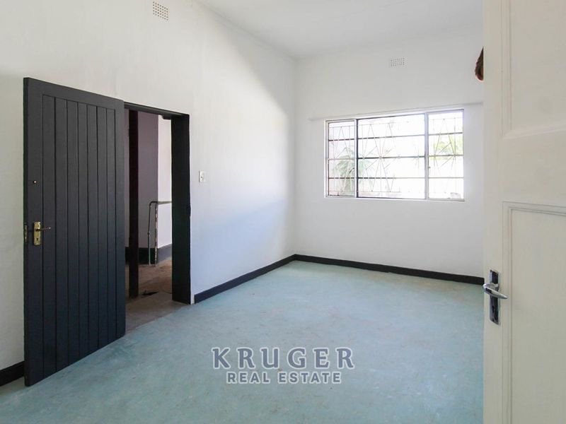 An empty bedroom featuring white walls, dark skirting boards, and a window with security bars.