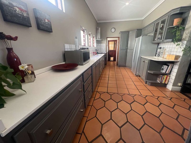 A well-maintained kitchen featuring grey cabinetry, white countertops, a tiled backsplash, and distinctive hexagonal terracotta floor tiles.