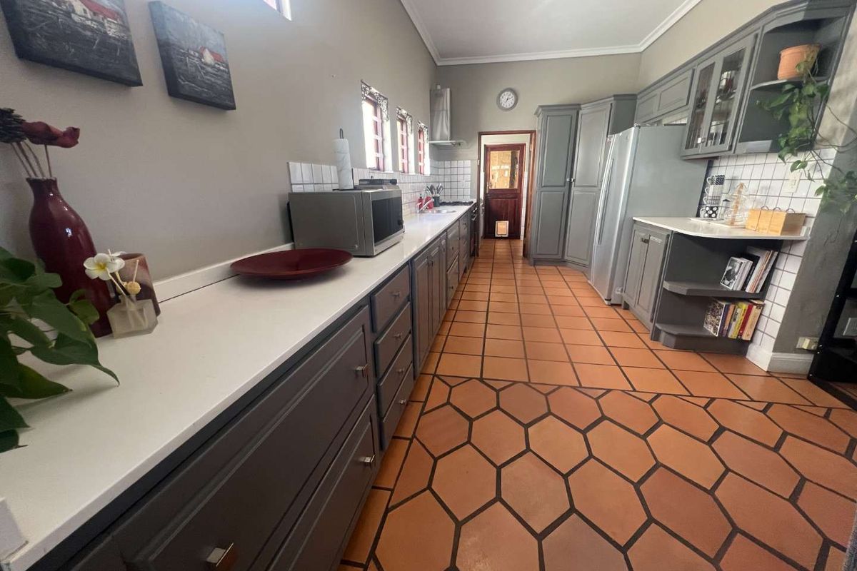 A well-maintained kitchen featuring grey cabinetry, white countertops, a tiled backsplash, and distinctive hexagonal terracotta floor tiles.
