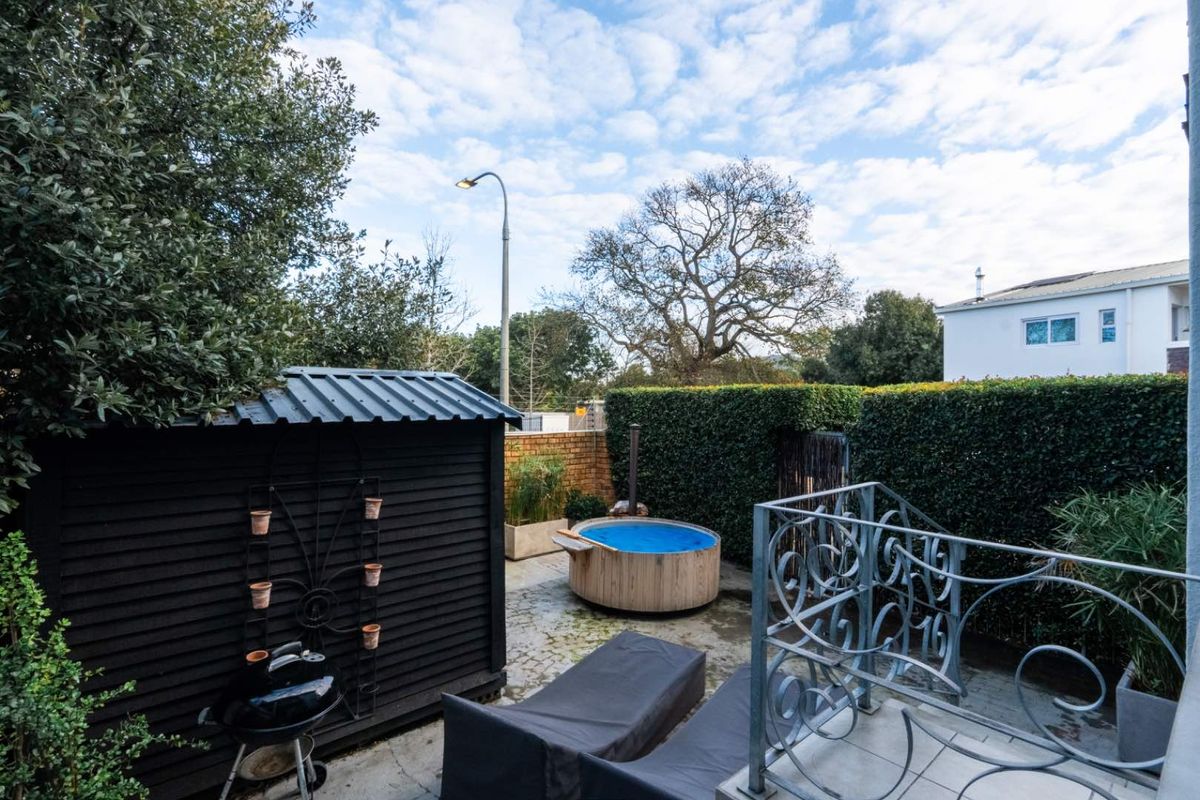 Private outdoor courtyard featuring a circular wooden hot tub, paved flooring, and established hedge screening for added privacy.