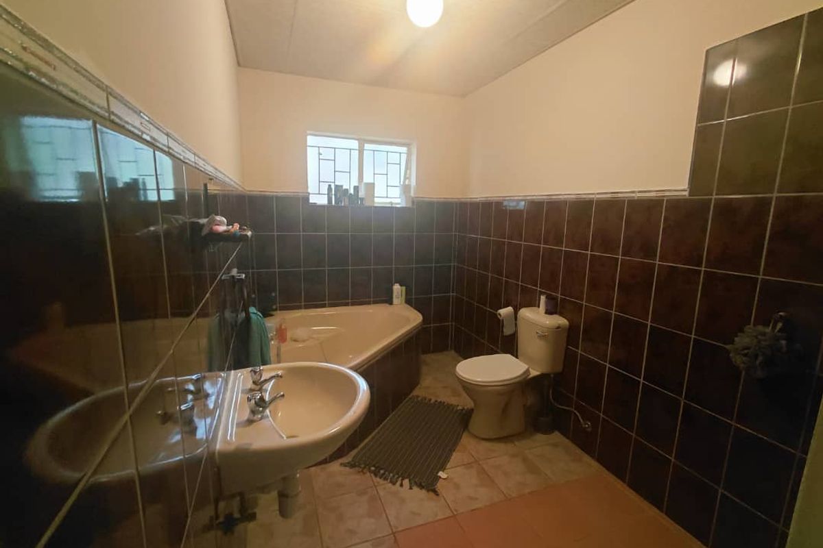 A dated bathroom featuring a corner bathtub, pedestal basin, and toilet, finished with dark wall tiles and a drop-ceiling.