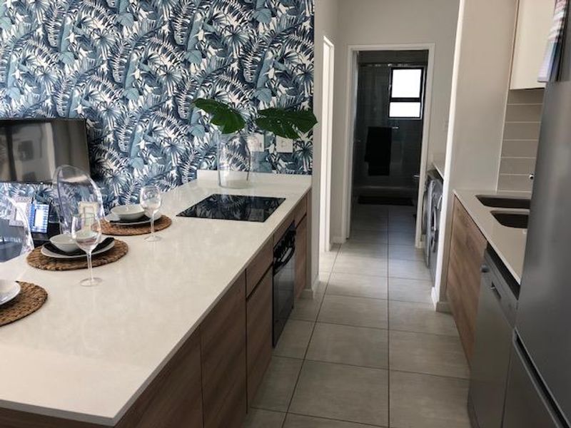 Modern open-plan kitchen featuring quartz countertops, built-in hob and oven, and sleek cabinetry, leading into a tiled utility area.