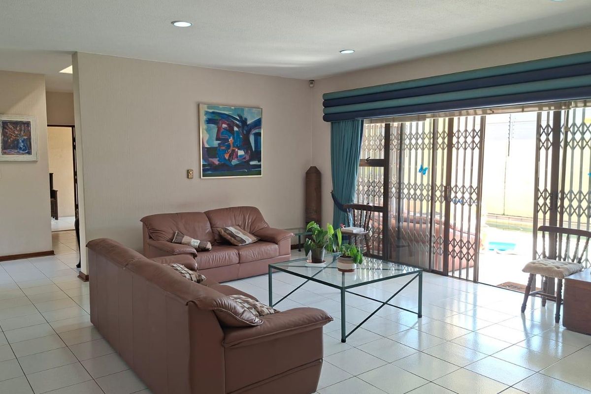 Spacious living room featuring ceramic floor tiles, recessed lighting, and large sliding glass doors with security gates leading to the outdoor area.
