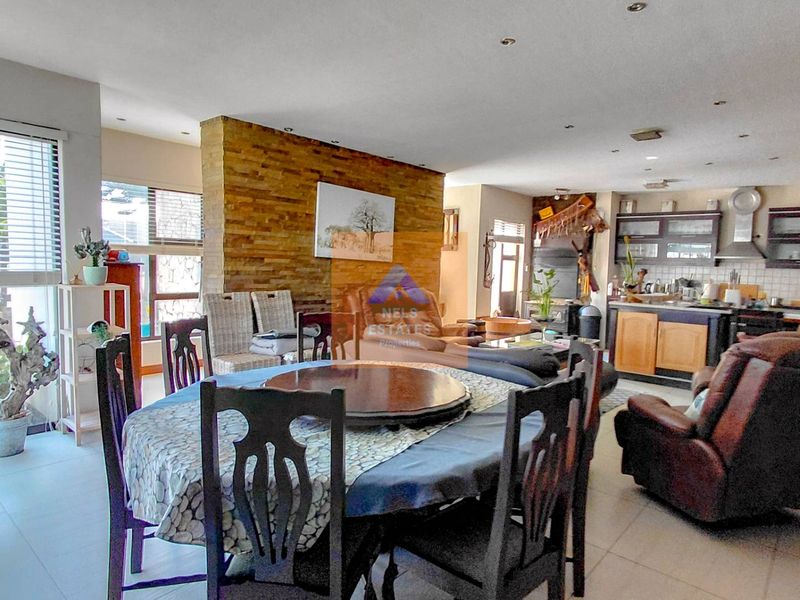 Open-plan living and dining area featuring a stone accent wall, tiled flooring, and an integrated kitchen with built-in cabinetry and modern lighting.