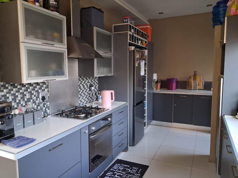 Modern kitchen featuring grey cabinetry, mosaic tile backsplash, gas hob, built-in oven, and tiled flooring with ample counter space.