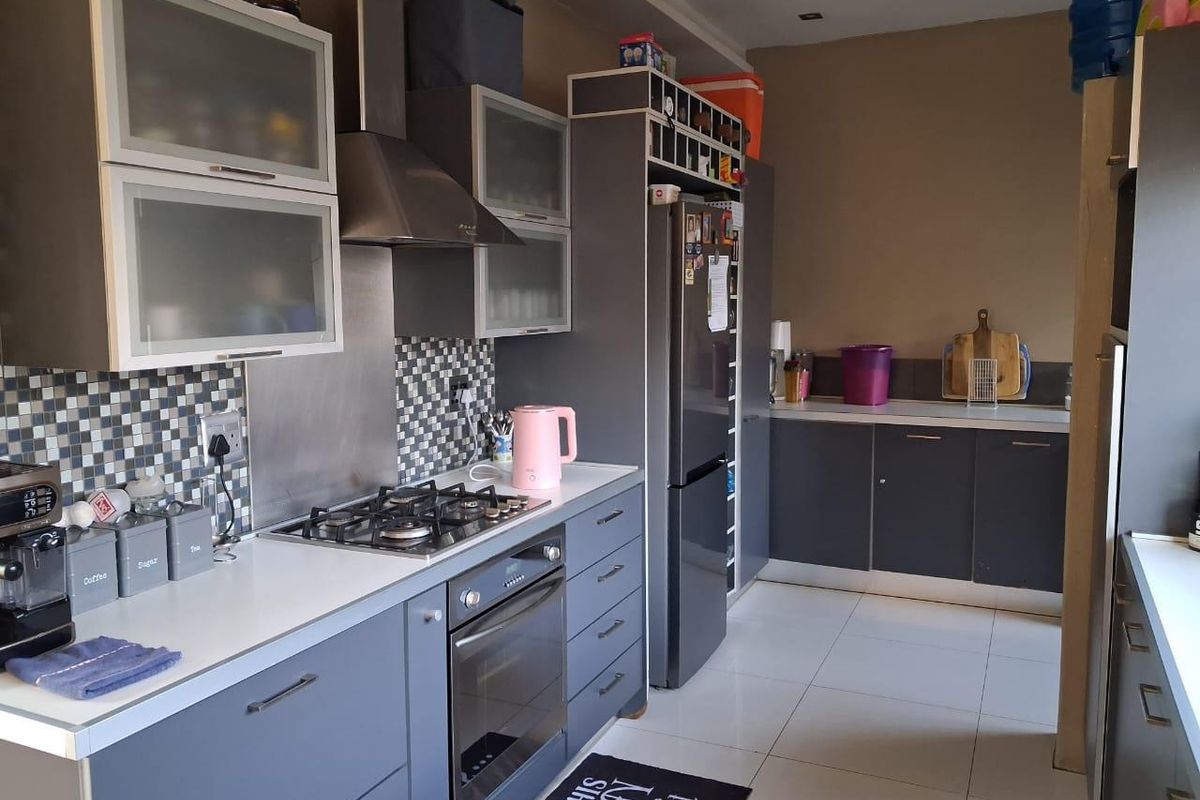 Modern kitchen featuring grey cabinetry, mosaic tile backsplash, gas hob, built-in oven, and tiled flooring with ample counter space.