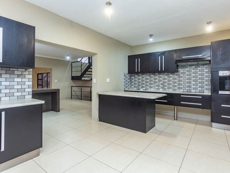 Modern kitchen featuring dark cabinetry, subway tile backsplash, built-in oven, extractor fan, and a central island, with tiled flooring throughout.