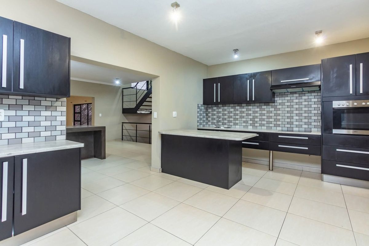 Modern kitchen featuring dark cabinetry, subway tile backsplash, built-in oven, extractor fan, and a central island, with tiled flooring throughout.