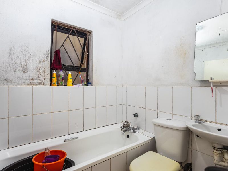 A dated bathroom featuring a bathtub, pedestal basin, and toilet, requiring significant cosmetic renovation and wall repairs to restore its condition.