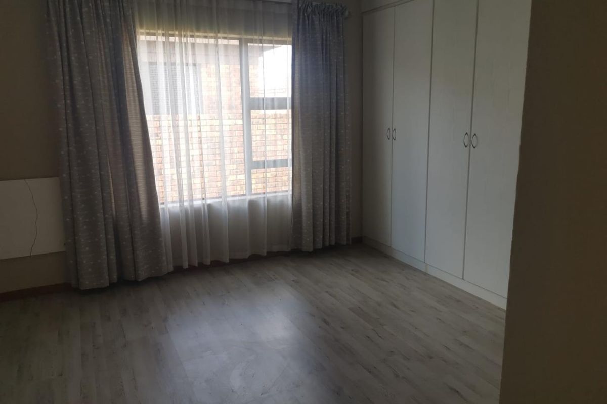 A bright, empty bedroom featuring light-toned laminate flooring and ample built-in cupboard storage space.