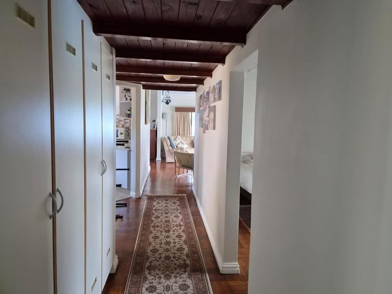 A hallway featuring parquet flooring, built-in storage cupboards, and exposed timber ceiling beams, providing access to adjacent living and bedroom areas.