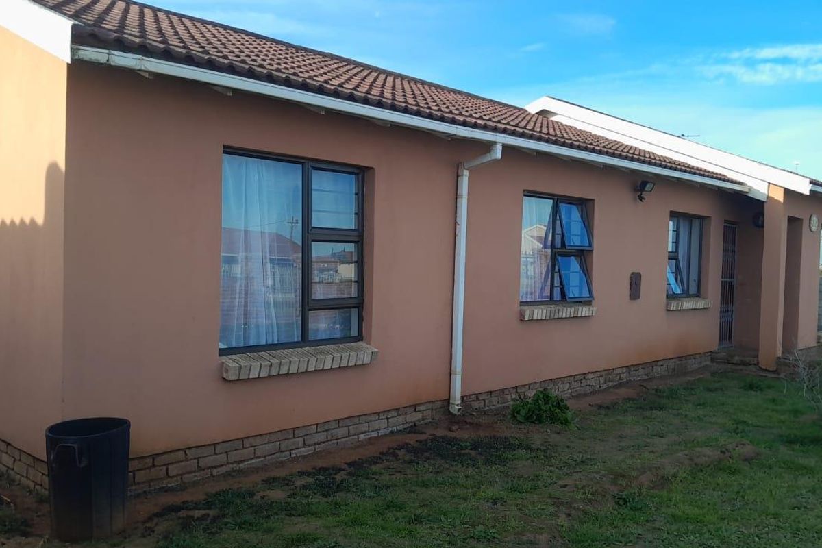 Rear view of a single-story residential house featuring a tiled roof, brick plinth, and aluminium window frames.