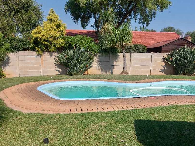 A private backyard featuring a swimming pool with brick coping, surrounded by a well-maintained lawn and a secure precast concrete boundary wall.