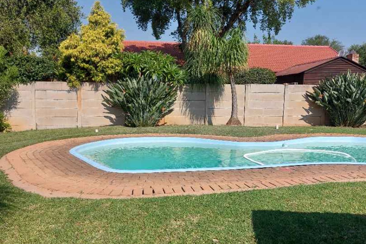 A private backyard featuring a swimming pool with brick coping, surrounded by a well-maintained lawn and a secure precast concrete boundary wall.