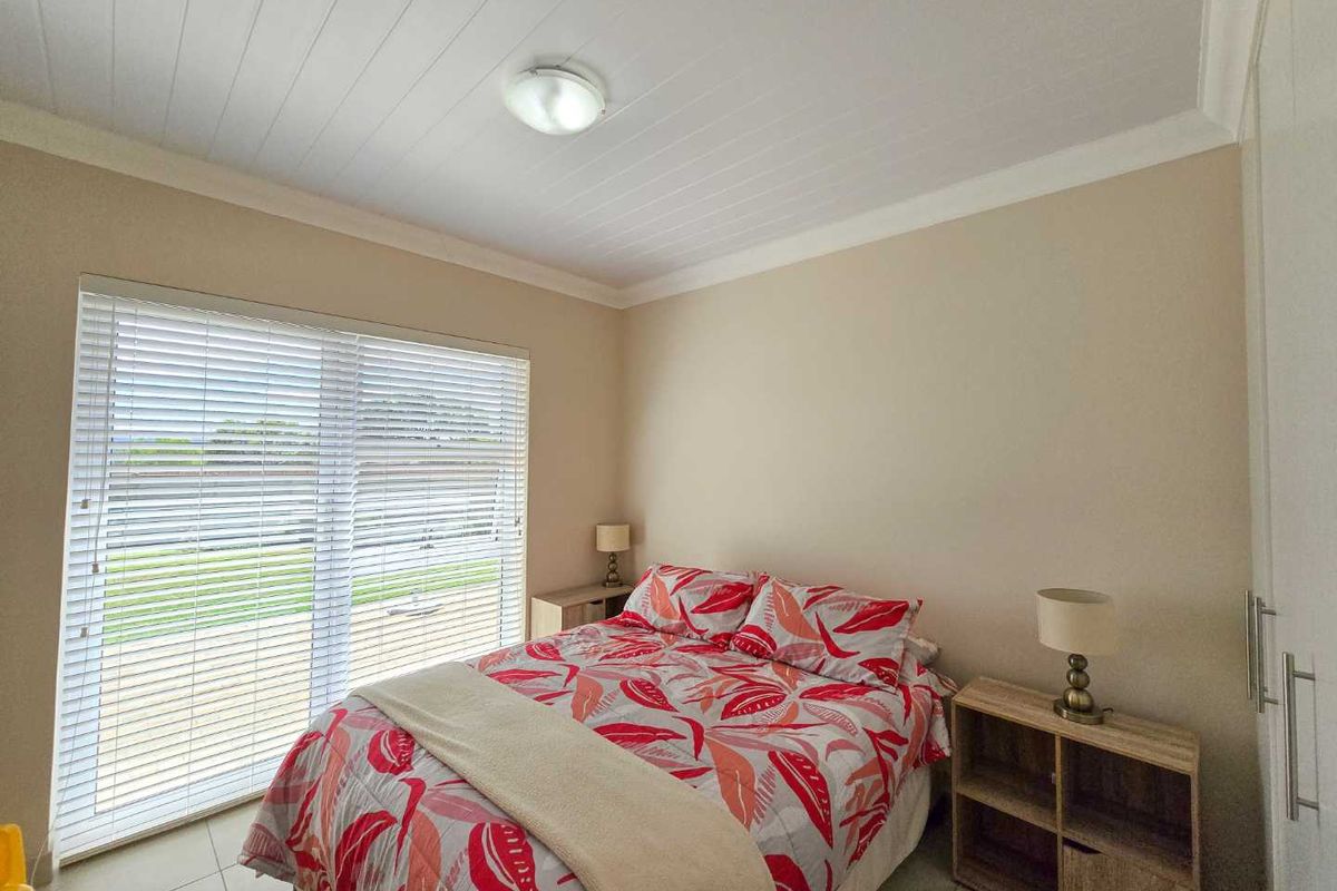 A well-lit bedroom featuring tiled flooring, built-in cupboards, and large windows fitted with horizontal blinds, offering a clean and functional living space.