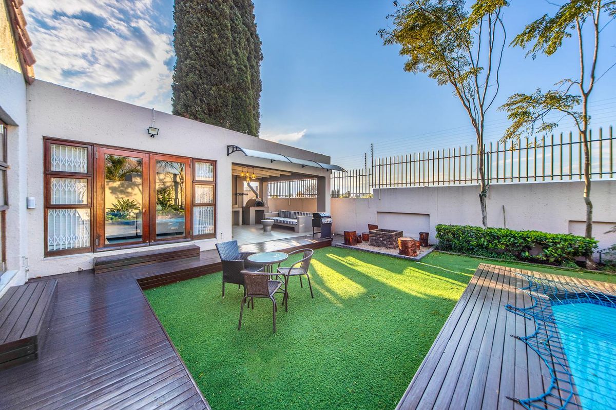 A well-maintained rear garden featuring wooden decking, a swimming pool, a covered patio area with a built-in braai, and secure perimeter fencing.