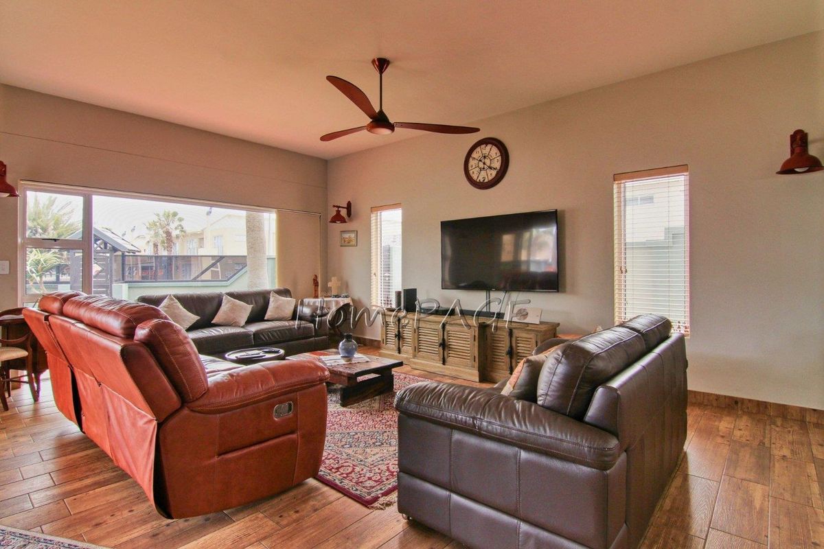Spacious living room featuring wood-look tile flooring, a ceiling fan, and large windows providing ample natural light.