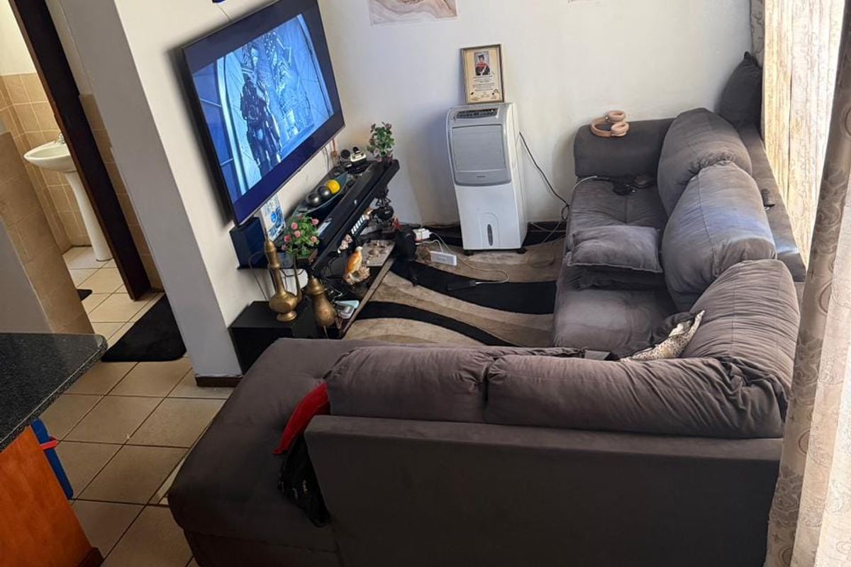 A compact living room featuring tiled flooring and a wall-mounted television, with direct access to an adjacent bathroom area.