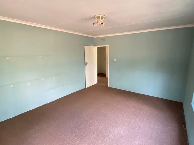 An empty bedroom featuring carpet flooring, security bars on the window, and a ceiling light fixture, ready for renovation or staging.