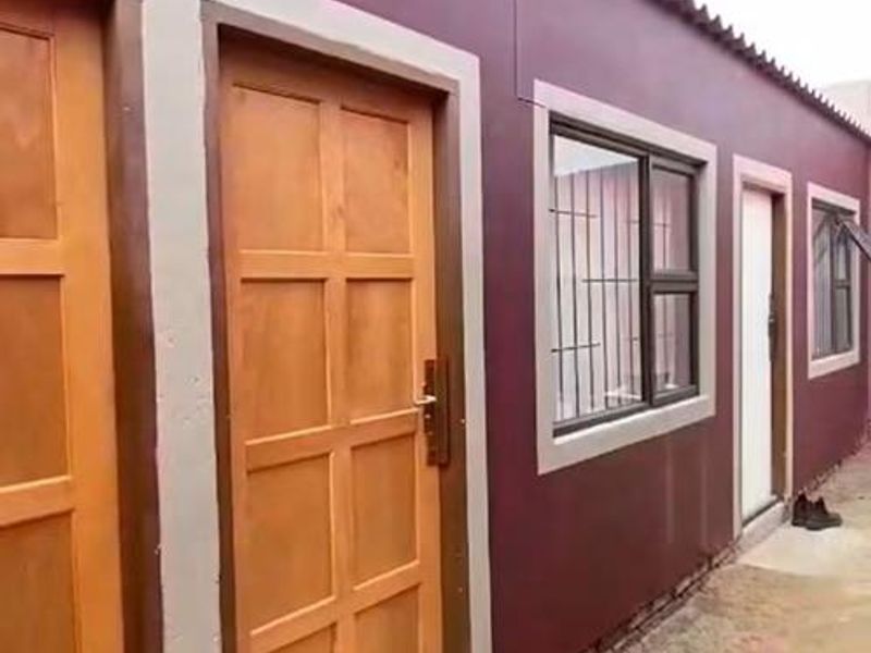 Exterior view of the rear facade featuring timber panel doors, aluminium windows with security bars, and corrugated roof sheeting.