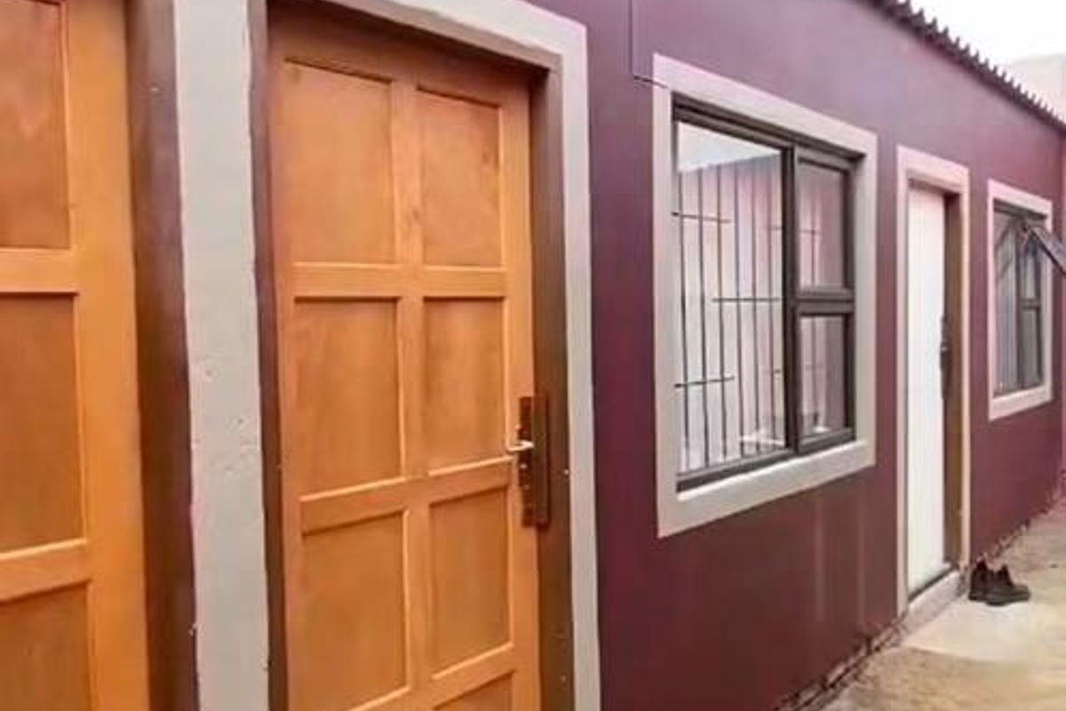 Exterior view of the rear facade featuring timber panel doors, aluminium windows with security bars, and corrugated roof sheeting.