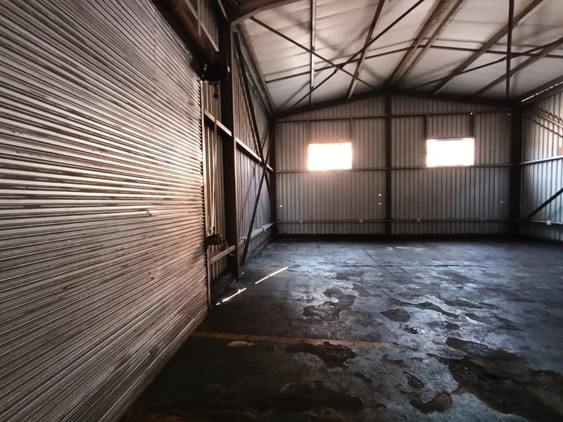 Spacious industrial utility area featuring corrugated metal walls, exposed steel roof trusses, a large roller shutter door, and a concrete floor.