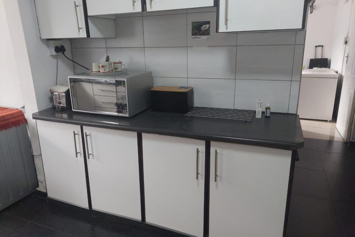 A functional kitchen area featuring white cabinetry, dark laminate countertops, and a tiled backsplash, providing essential storage and workspace.