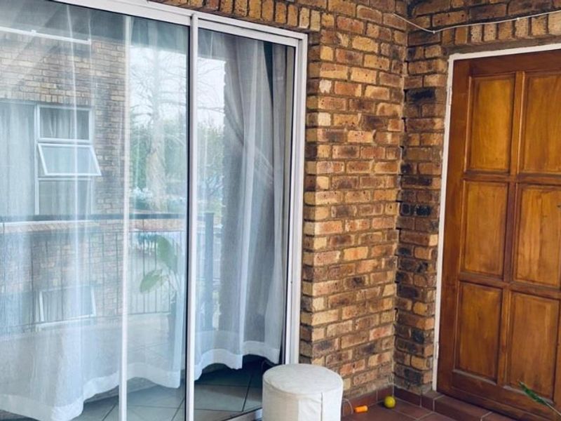 A covered balcony area featuring exposed brick walls, tiled flooring, and a sliding glass door providing access to the interior.
