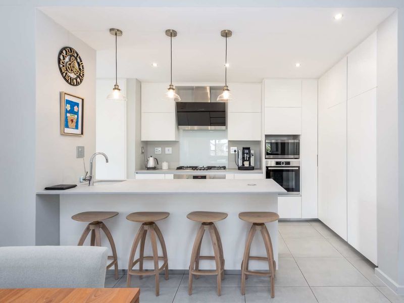 Modern kitchen featuring a central island with breakfast bar, integrated appliances, sleek handleless cabinetry, and contemporary pendant lighting.