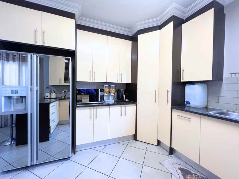 A functional kitchen featuring cream-colored cabinetry, dark granite countertops, tiled flooring, and ample storage space with a clean, modern layout.