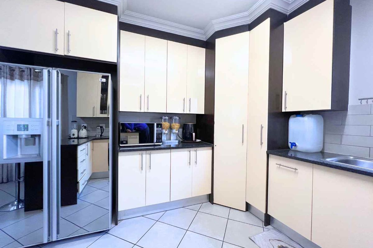 A functional kitchen featuring cream-colored cabinetry, dark granite countertops, tiled flooring, and ample storage space with a clean, modern layout.