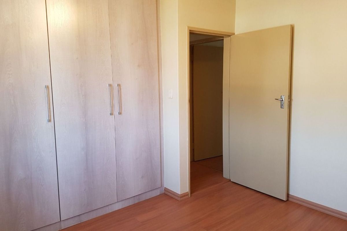 A bedroom featuring light wood-grain built-in cupboards, laminate flooring, and a neutral interior finish with access to the hallway.