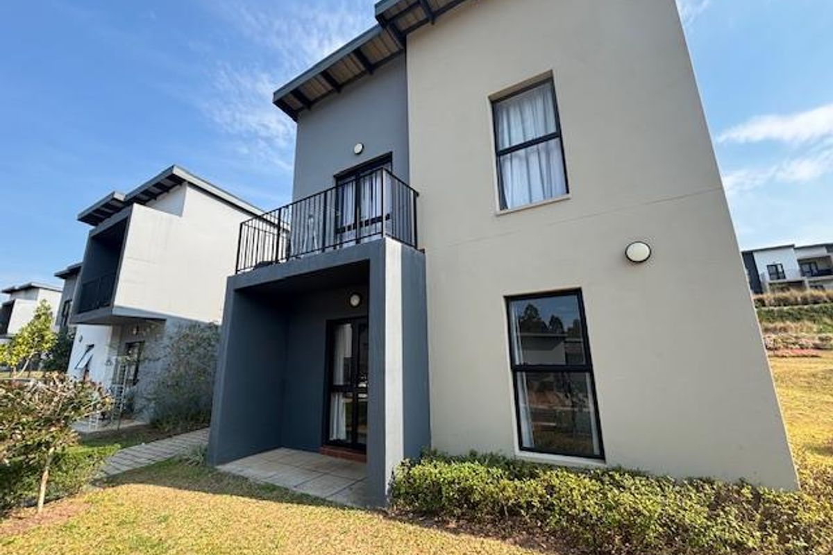 Rear view of a modern two-story apartment building featuring a ground-floor patio, a first-floor balcony with metal railings, and landscaped garden area.